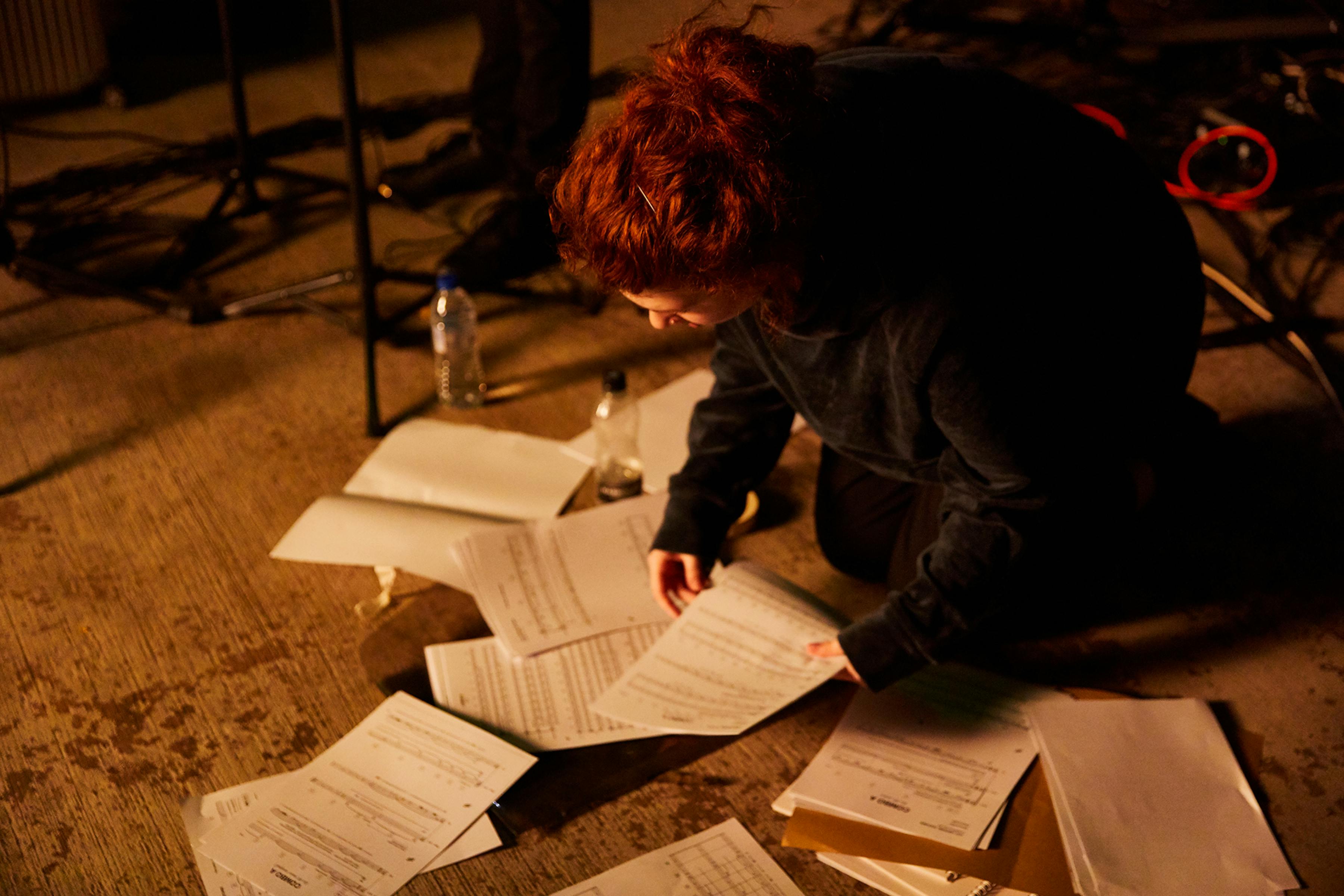 A woman kneeling over sheets of manuscript paper